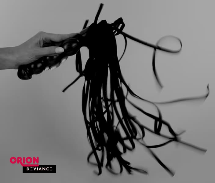 A black flogger with long, soft straps held by a hand.
