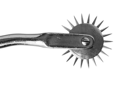 Close-up of a Wartenberg wheel on a white background: a metal handle with a spiked rotating wheel
