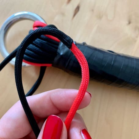 The finished handle wrapped in black insulating tape, with a hand guiding a red cord along it to weave the grip