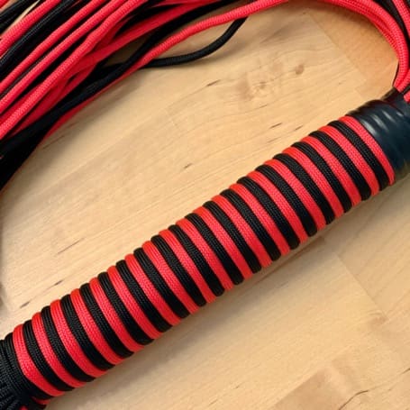 Finished flogger handle wrapped in even black and red bands, with the falls lying behind it