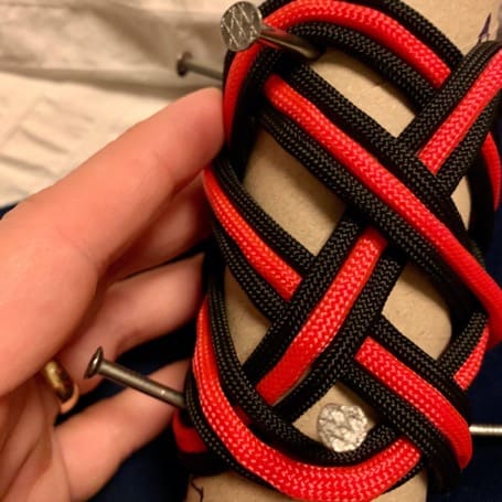 Black and red paracord woven over the nails on the cardboard tube into a braided pattern