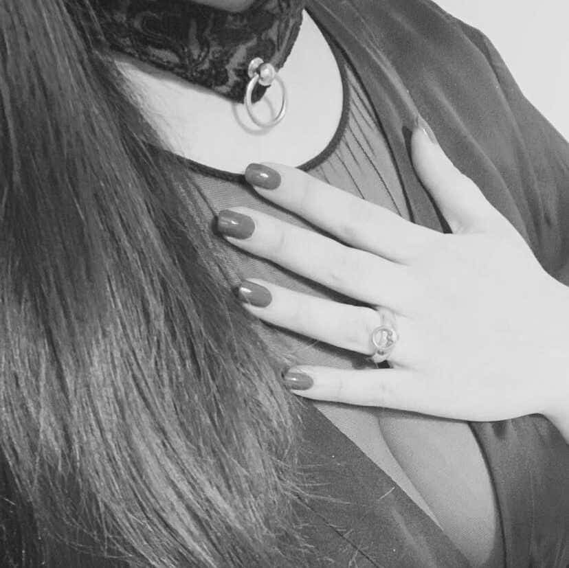 Black and white close-up of a hand resting on the chest over a sheer blouse, with a lace collar and O-ring at the neck
