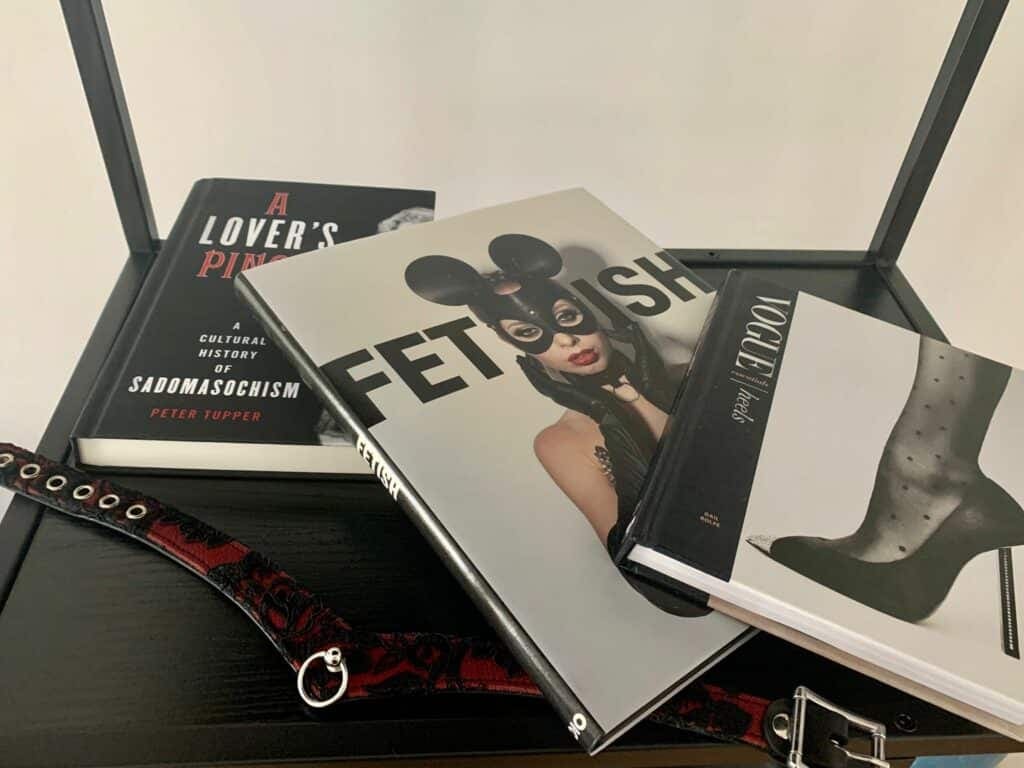 Photo books on fetish and sadomasochism on a black shelf — “Fetish”, “A Lover's Pinch” and “Vogue Essentials: Heels” — beside a red and black collar