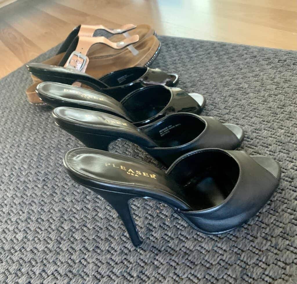 Four pairs of black Pleaser heels and mules lined up on a grey carpet