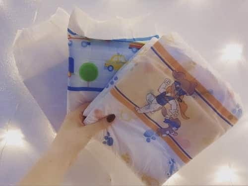 A hand holding up two printed nappies side by side, one with cars and one with dogs