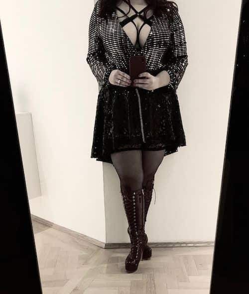 Mirror selfie in a sequinned jacket, black harness, skirt and laced platform boots