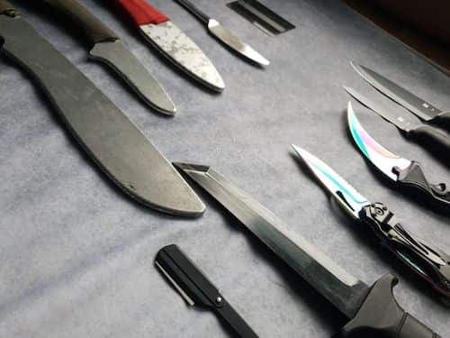 A collection of assorted knives and blades laid out side by side on a grey surface