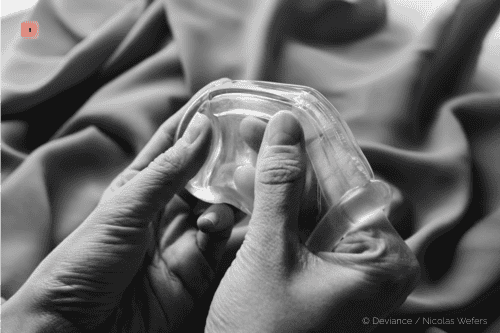 Black and white close-up of two hands holding a clear silicone chastity cage
