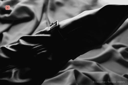 Black and white close-up of a black monoglove with a buckle on shiny fabric
