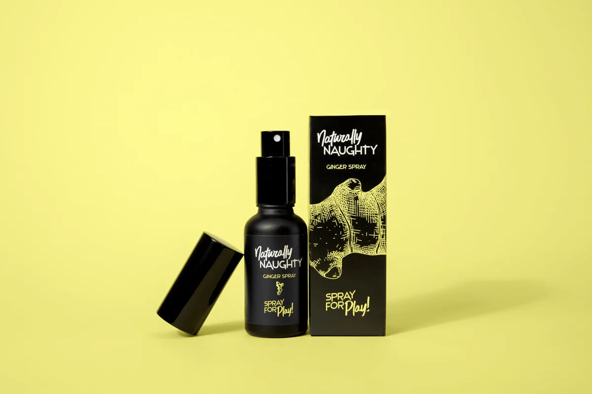 Black “Naturally Naughty Ginger Spray” bottle beside its packaging on a yellow background